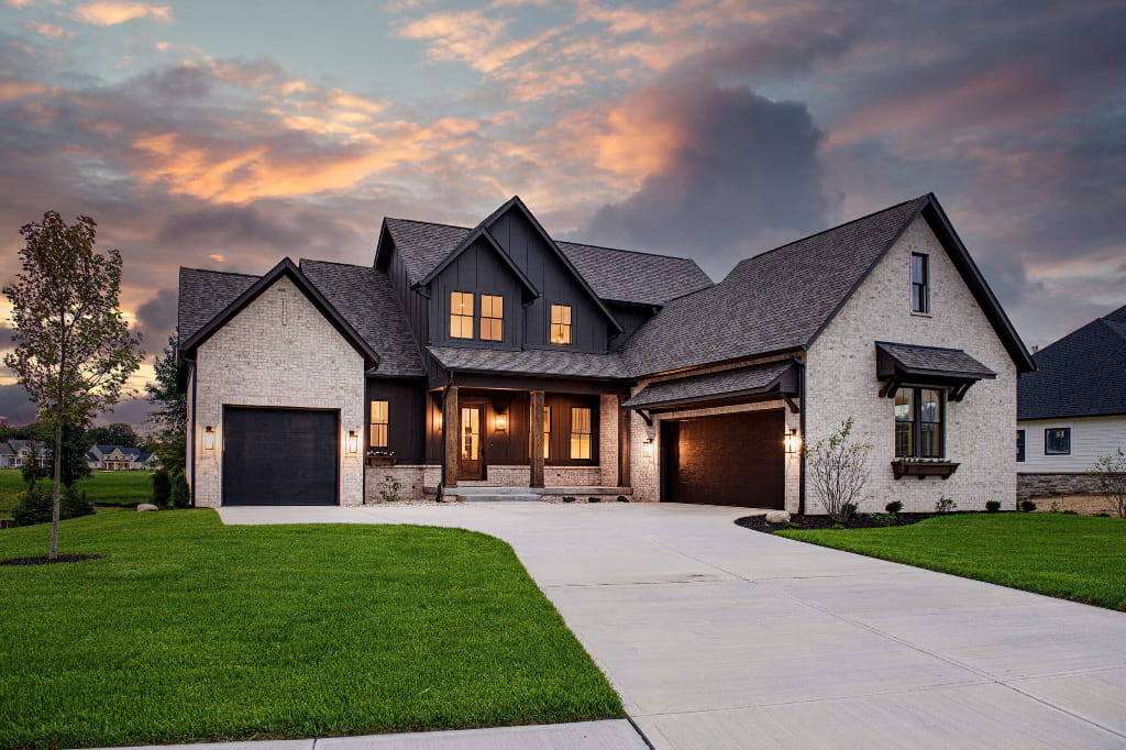 Newly built custom home with modern farmhouse exterior, brick and dark siding, two-car garage, and wide driveway at sunset in Sun Prairie, WI.