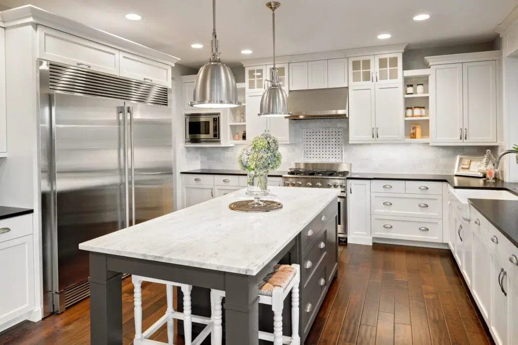 Updated white kitchen with shaker cabinets, large island with stone countertop, stainless steel appliances, and modern pendant lighting in Sun Prairie, WI.